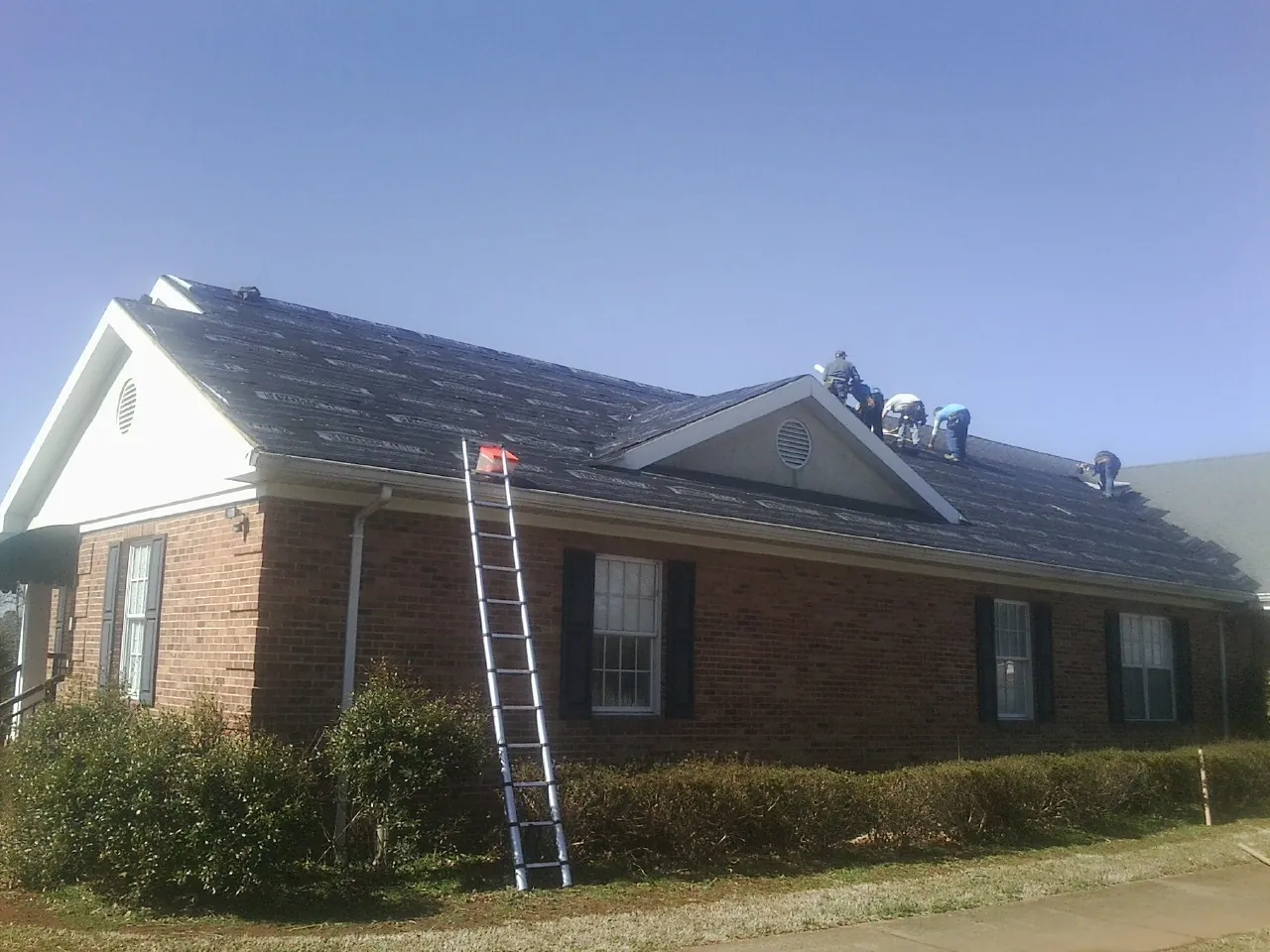 Crew tearing shingles off a brick ranch roof with a ladder set — Metal Roof Repair work by our crew in Society Hill