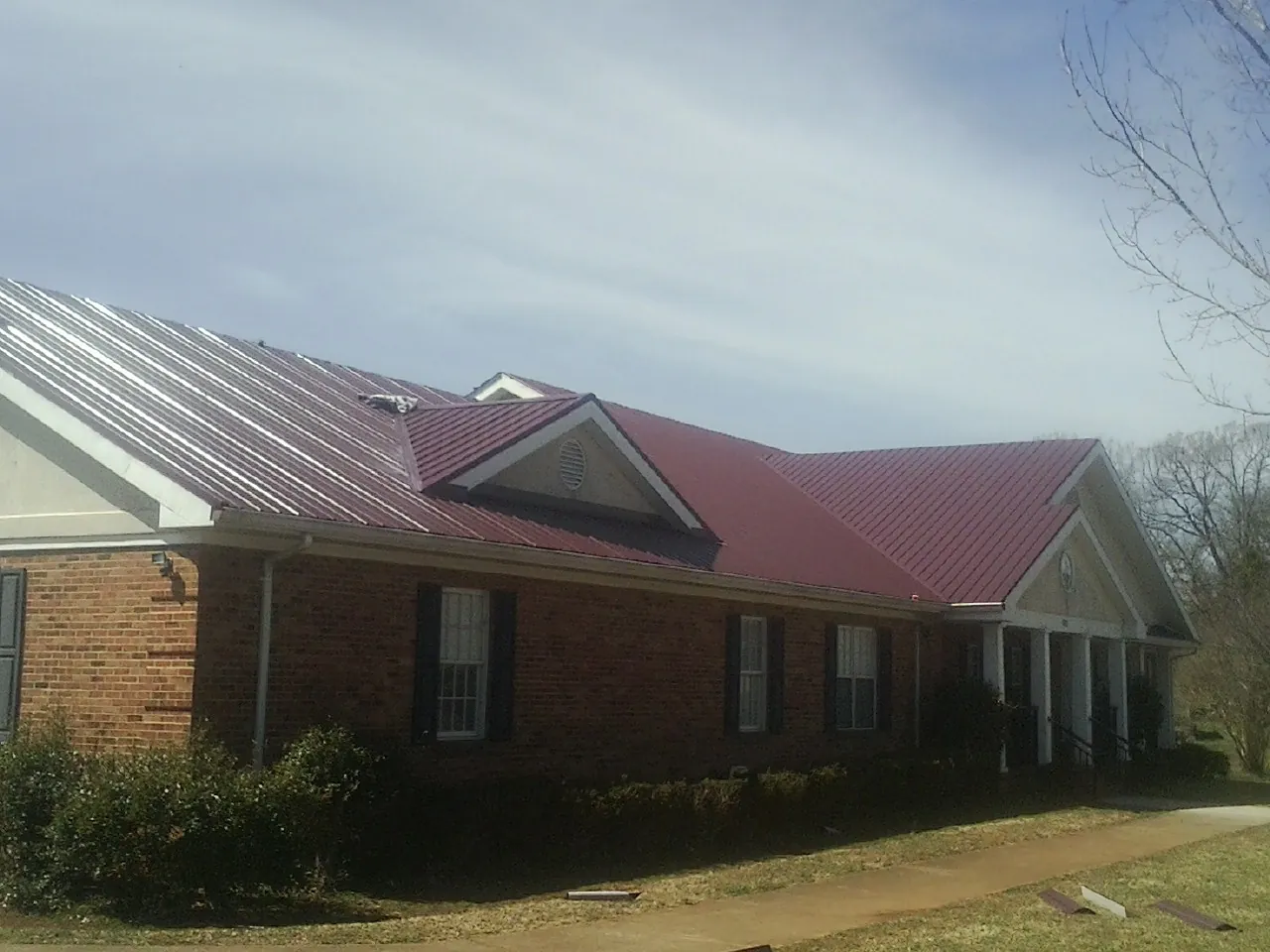 Red metal roof with gabled entries on a long brick building, from a Hail Damage Roof Repair job in Society Hill