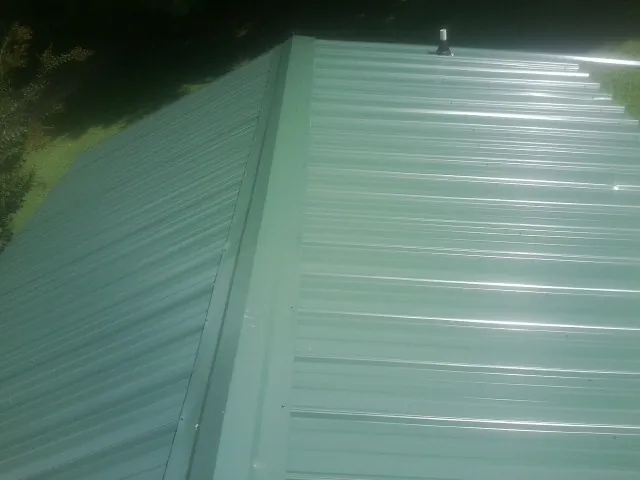 New green metal panels meeting at the ridge of a roof — Flat Roof Repair work by our crew in Society Hill