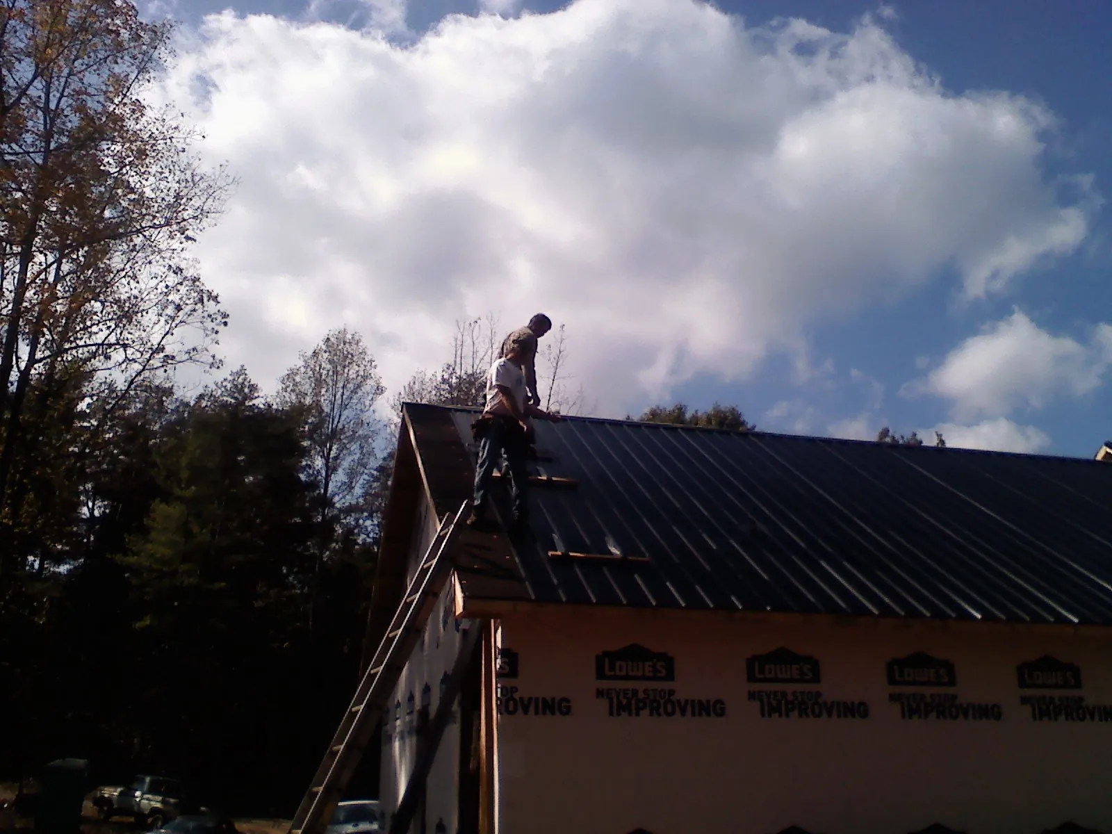 Roofer fastening dark metal panels high against a cloudy sky, from a Roof Inspection job in Society Hill