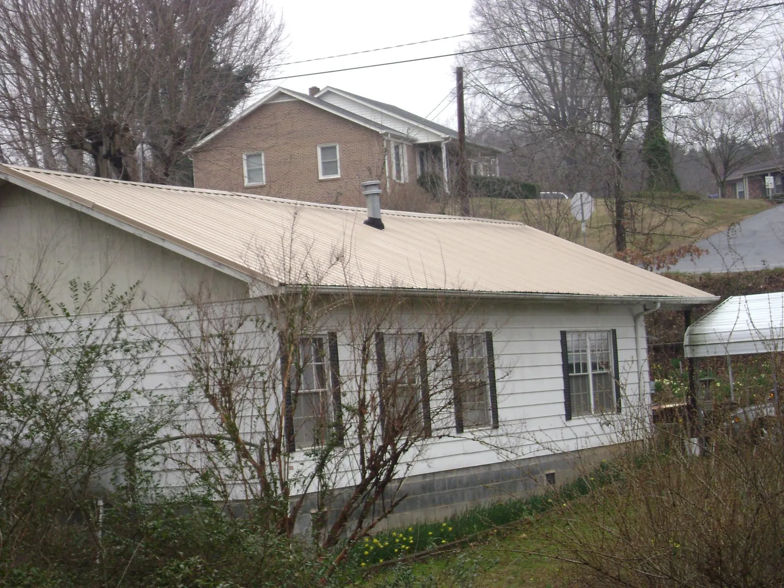 Tan metal roof on a white sided house set into a hillside — Commercial Roofing by Roofing Brothers in Society Hill